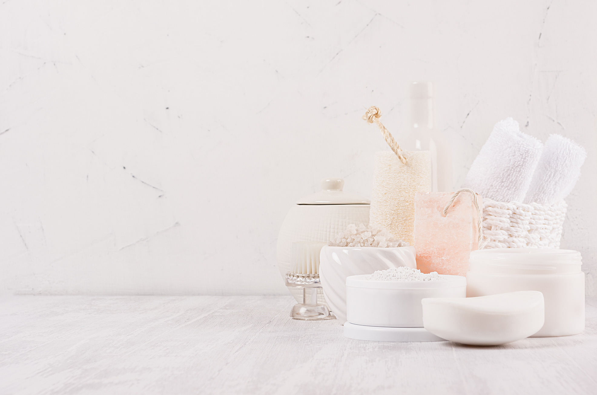 Handicraft natural cosmetics - white cream, soap, clay,  towel, pink salt and bath accessories on soft light white wood table, copy space.